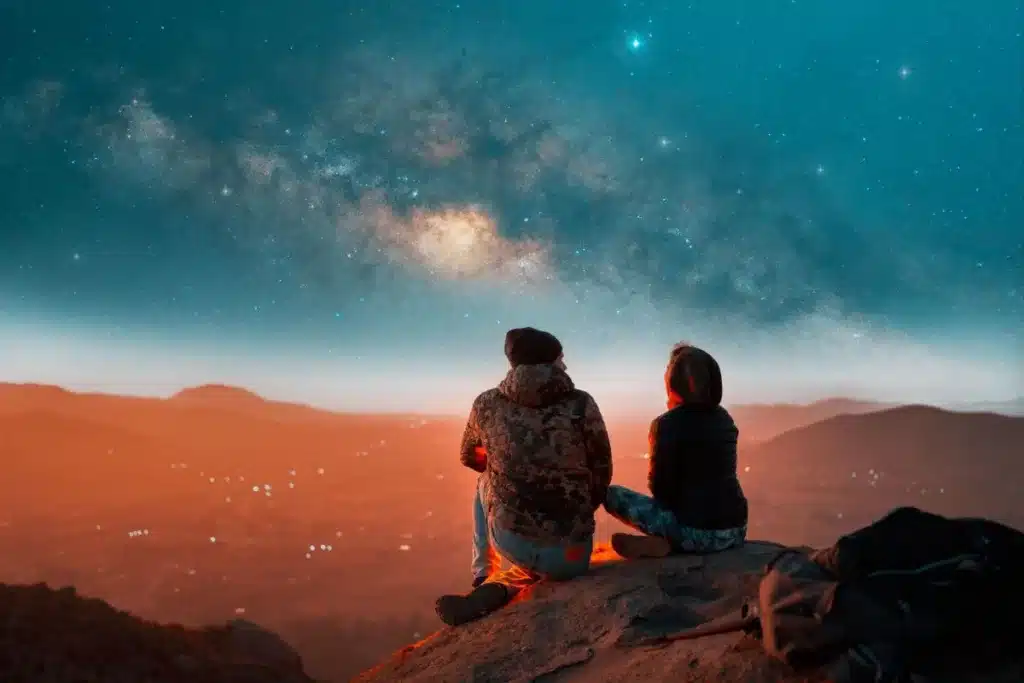 Two people sitting beneath the Milky Way, representing connection and shared reflection.