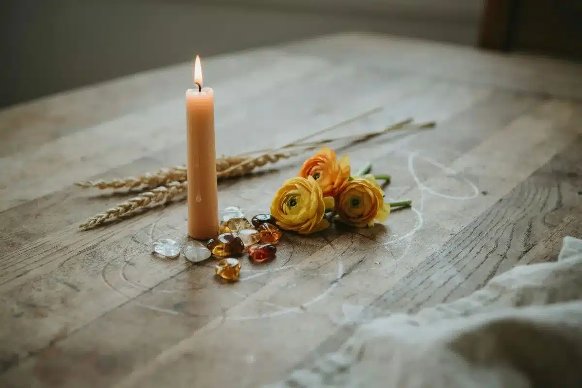 Yellow Candle Spiritual Meaning Glowing yellow candle surrounded by flowers and natural stones.
